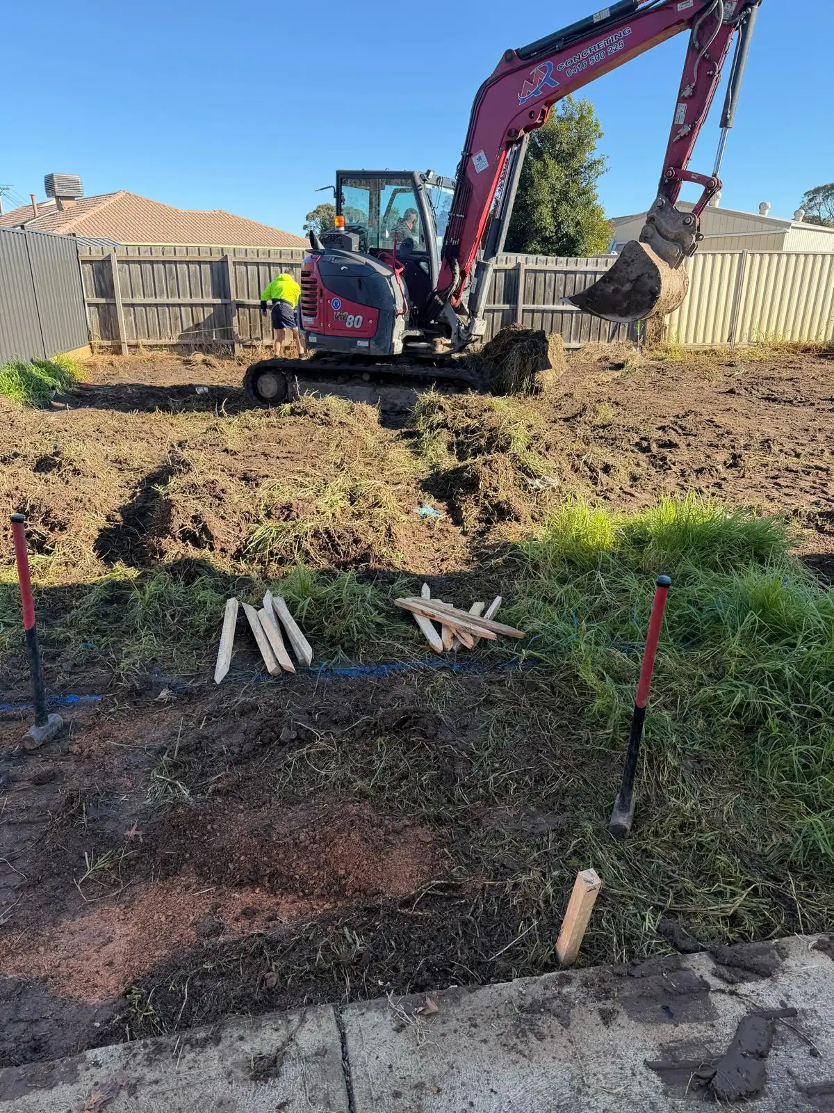 Excavator clearing and levelling the block, with set-out pegs in the ground